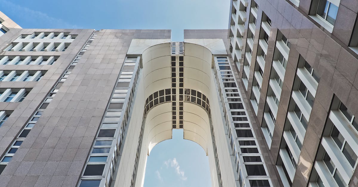 Low angle view of modern skyscraper with futuristic arch against blue sky.