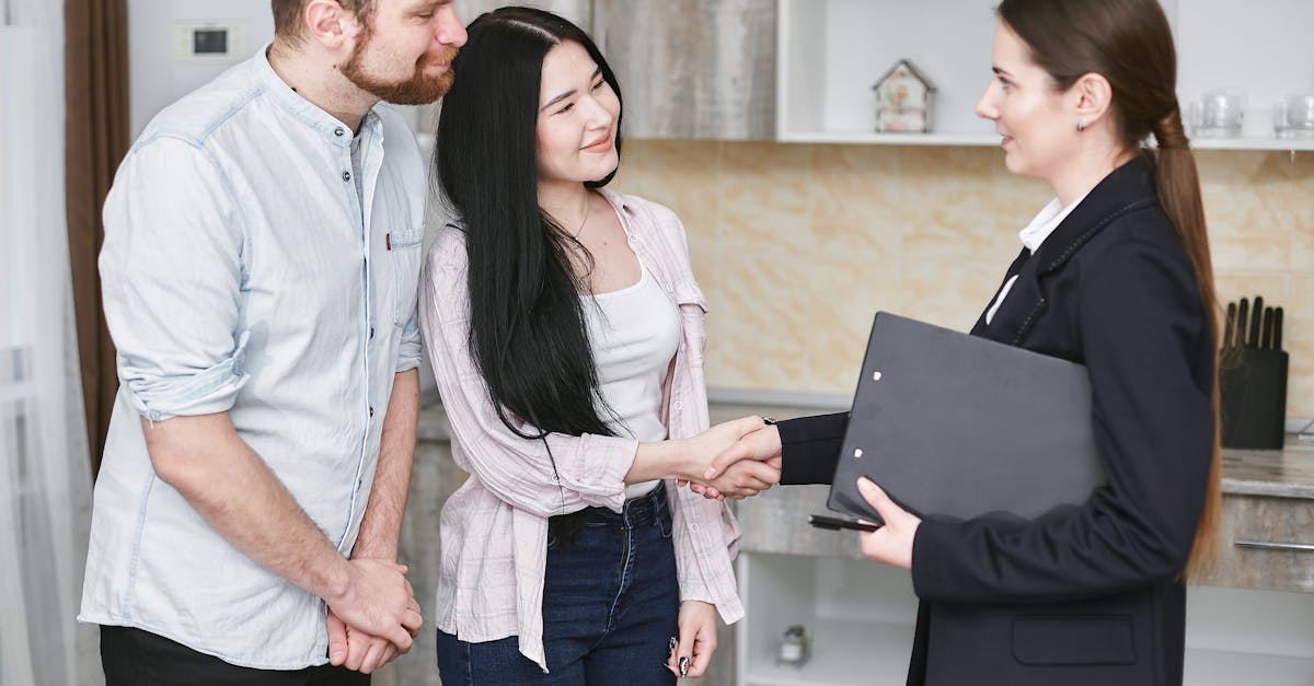 A young couple shakes hands with a real estate agent during a home tour or negotiation in a modern setting.
